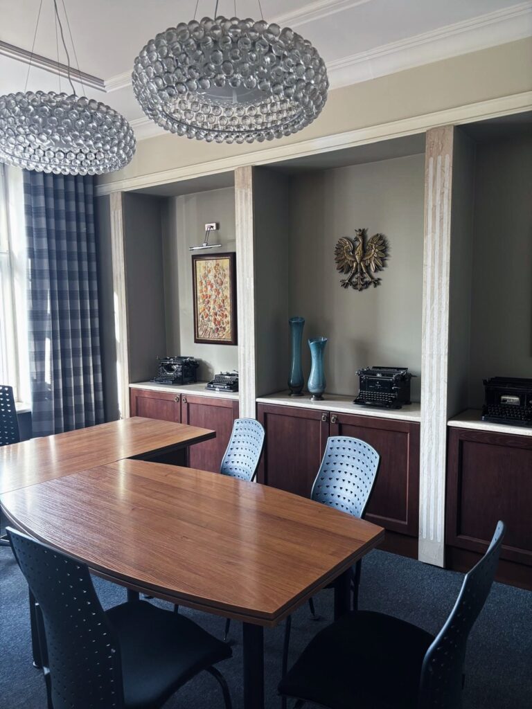 Sala czynności - stół, zabudowa z maszynami do pisania i godłem RP, krzesła